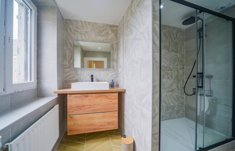 Baño moderno con ducha, lavabo sobre mueble de madera y paredes de azulejos claros.