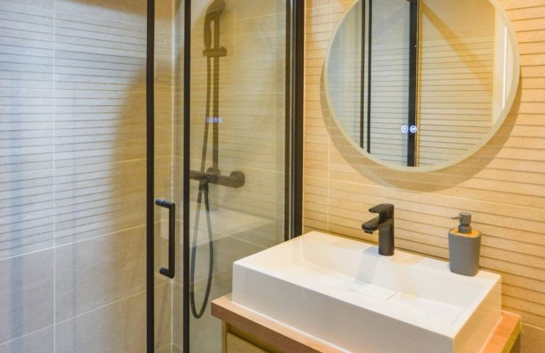 Baño moderno con ducha de cristal, espejo redondo y elegante lavabo.