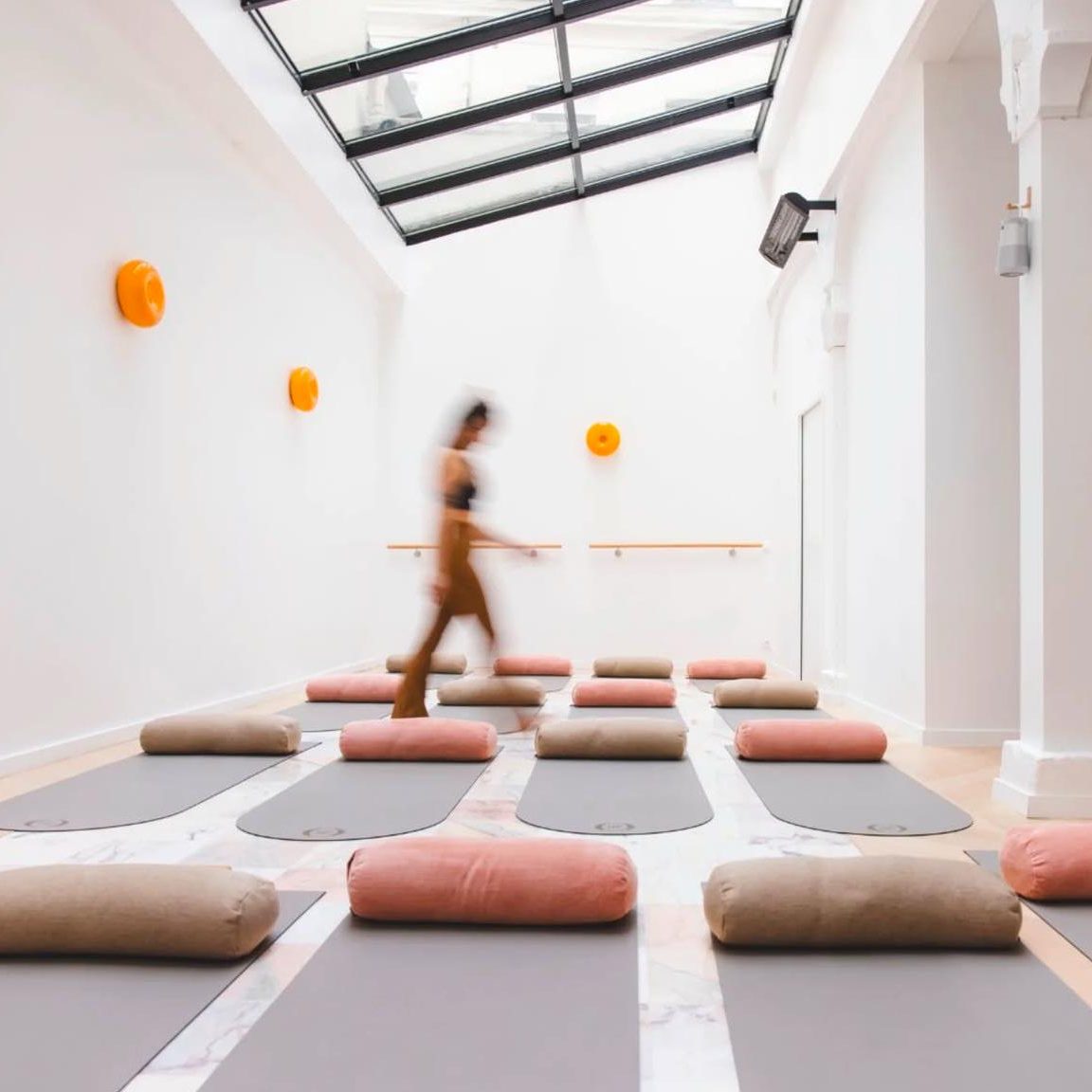 Salle de yoga claire avec des tapis et des coussins, une personne en mouvement.
