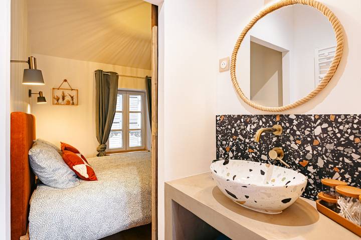 Salle de bain moderne avec lavabo en céramique, miroir rond et vue sur une chambre.