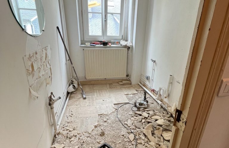 Interior de un pasillo en remodelación, con paredes dañadas y escombros en el piso.