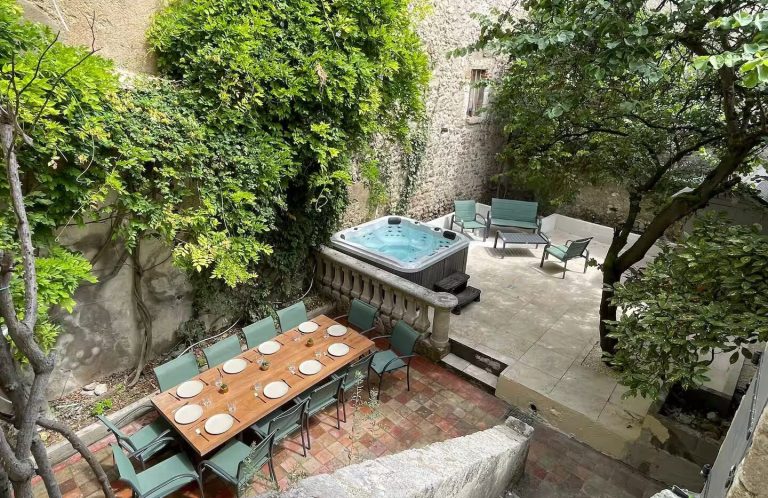 terraza sombreada con mesa de comedor y jacuzzi rodeado de vegetación.