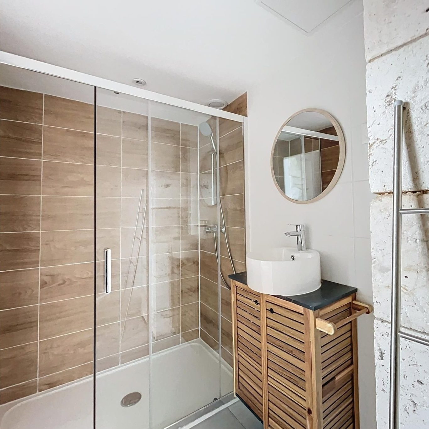 Salle de bains moderne avec douche en verre, lavabo rond et meuble en bois.