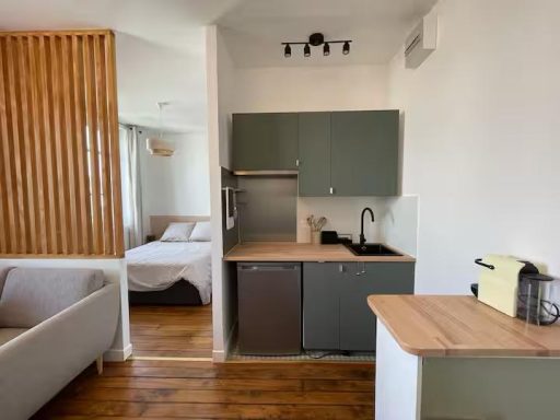 Cocina moderna con muebles grises y madera, vista de una sala al fondo.